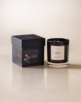 A black candle labeled 'NOITE' with a floral pattern on the packaging, presented next to its box on a light background.