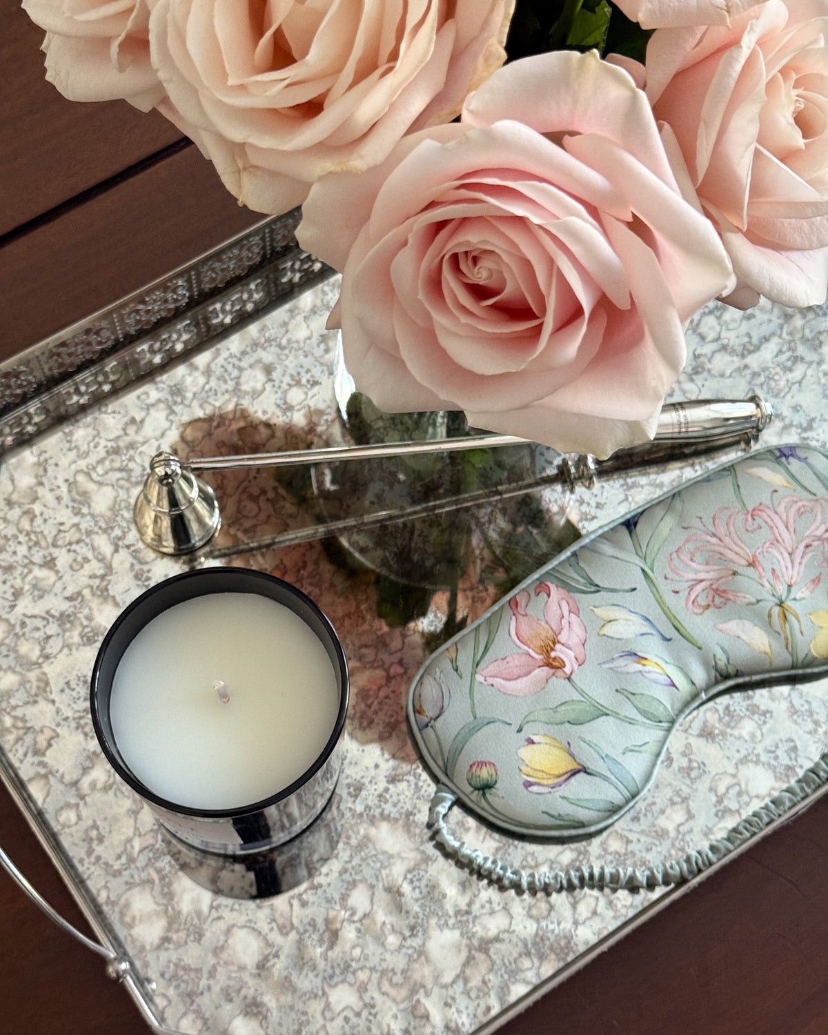Decorative tray with pink roses, a candle, and a handbag on a wooden surface.
