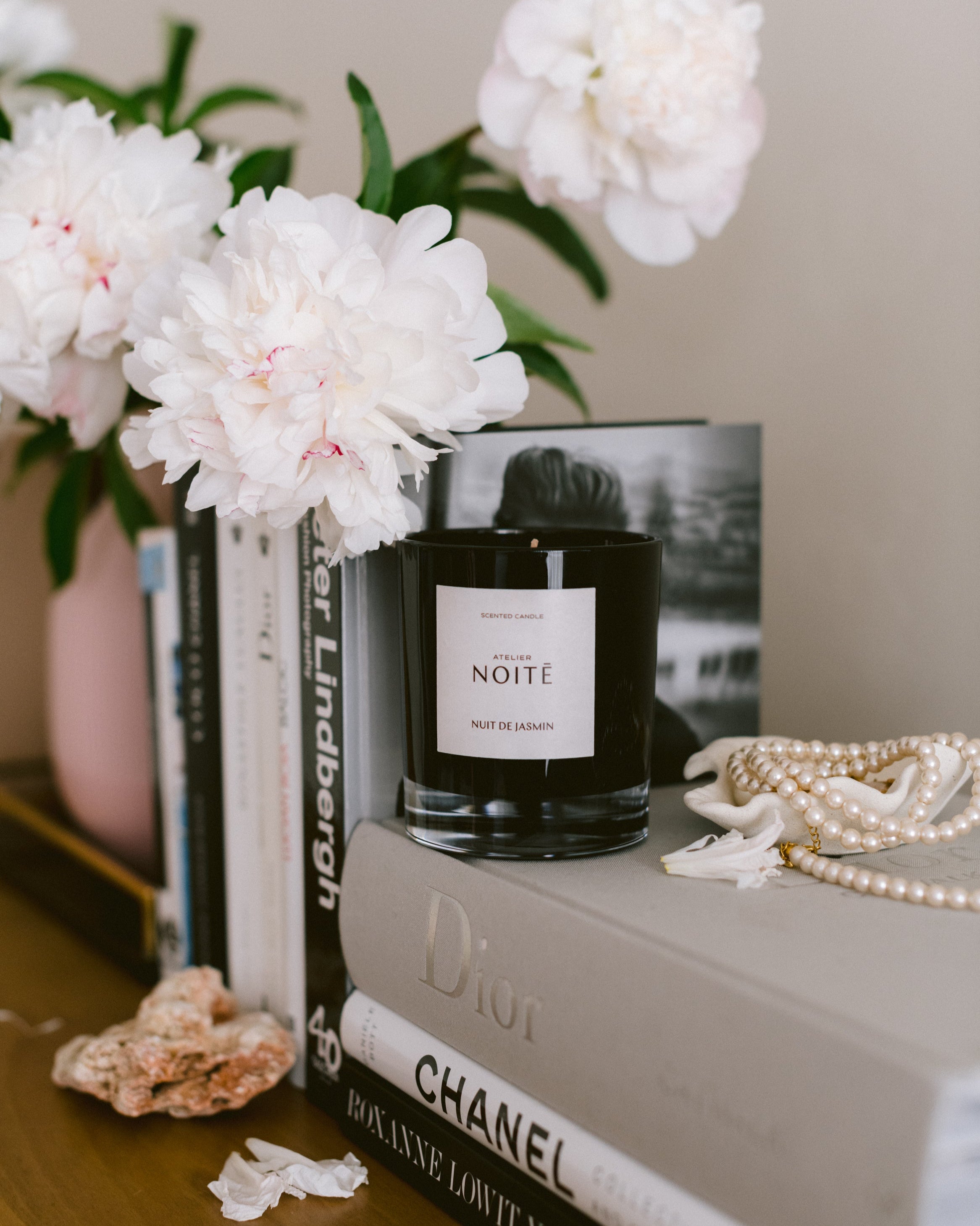 Candle labeled 'Noite' on books with white flowers and pearls.