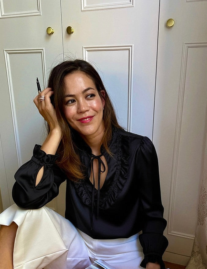 Woman in black blouse holding a pen sitting in front of a white background