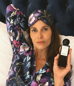 Image of a woman with a purple silk mask in a purple pajama holding a black home perfume bottle