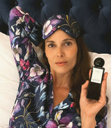 Image of a woman with a purple silk mask in a purple pajama holding a black home perfume bottle