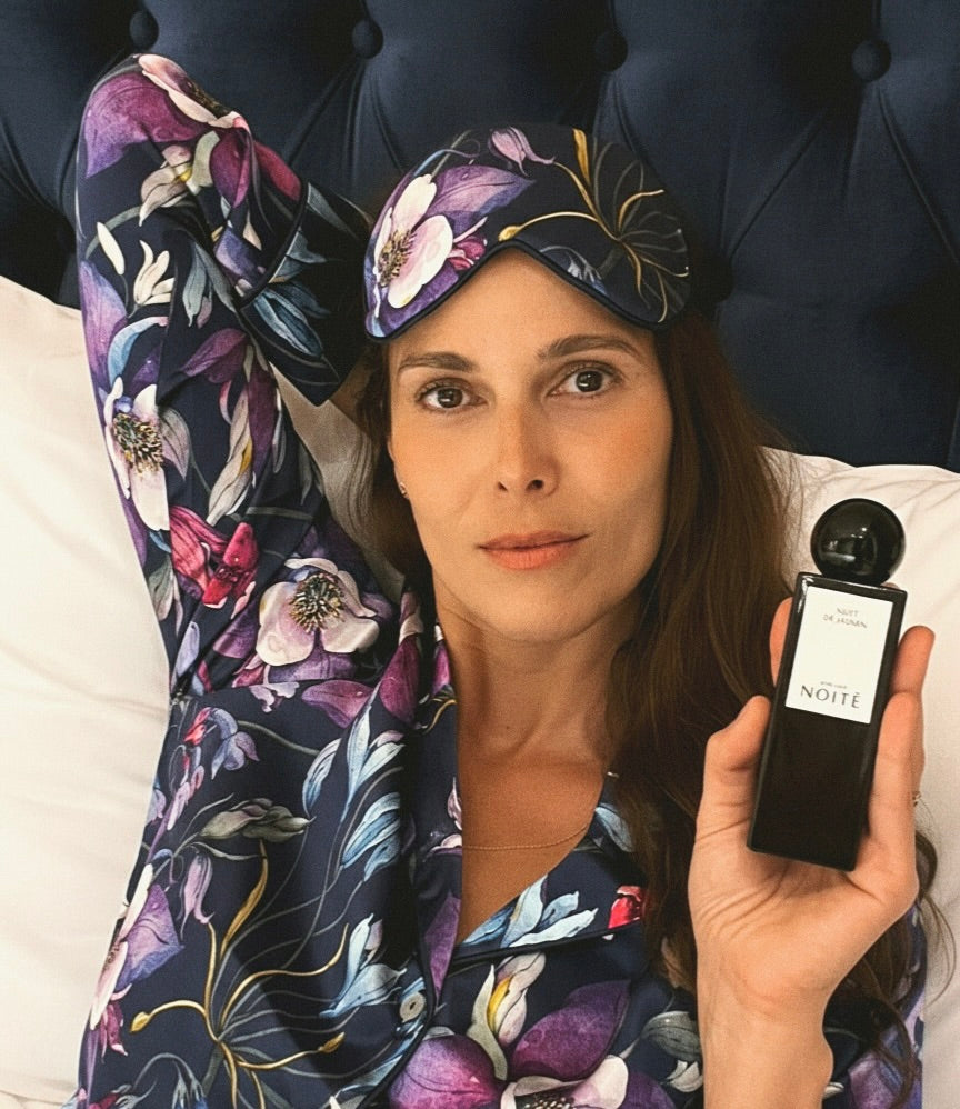 Image of a woman with a purple silk mask in a purple pajama holding a black home perfume bottle